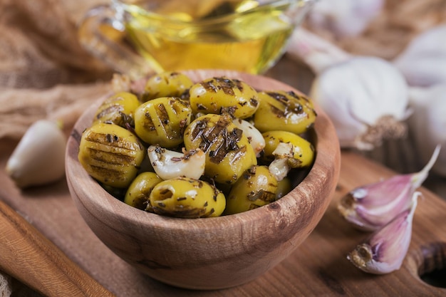 Gegrillte Oliven mit Knoblauch-Olivenöl und Gewürzen auf Holzhintergrund