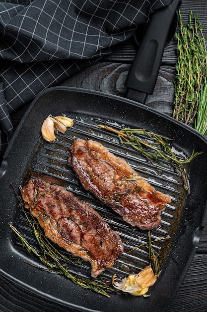 Gegrillte Prime Black Angus Rindersteaks Striploin oder New York in einer Grillpfanne. Dunkler hölzerner Hintergrund. Ansicht von oben.