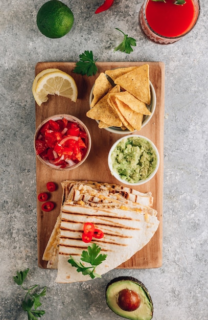 Gegrillte Quesadillas auf Holzbrett und mit Salsa und Guacamole auf Steinhintergrund. Konzept der mexikanischen Küche Quesadilla-Wrap mit Hühnchen und Mais. Ansicht von oben