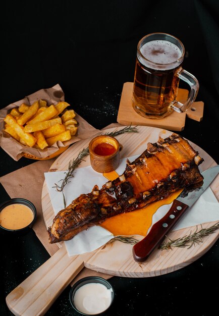 gegrillte Rippchen, begleitet von Pommes Frites und einem Getränk auf Holzbrettern auf schwarzem Hintergrund