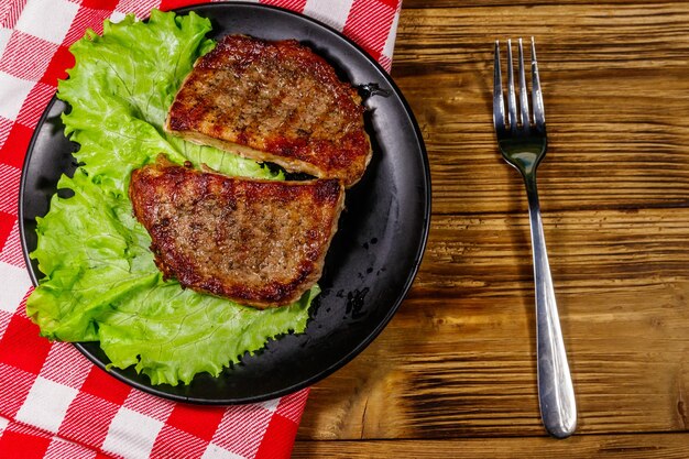 Gegrillte Schweinesteaks mit Salatblättern auf Holztisch Draufsicht