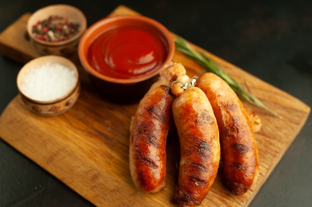 Gegrillte Würstchen mit Gewürzen, Ketchup und Rosmarin auf einem Steintisch, essfertig