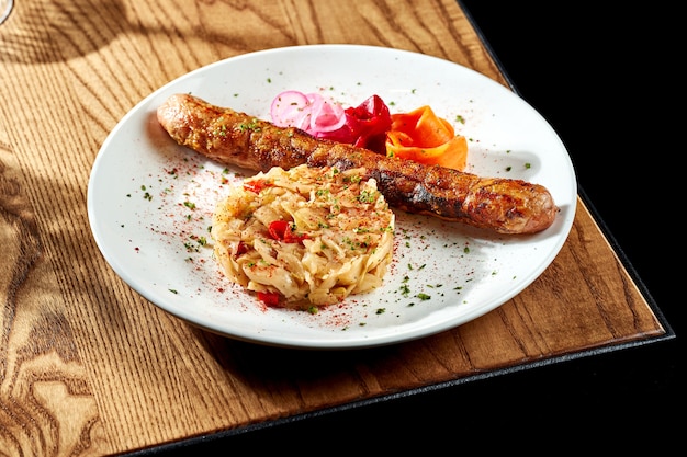 Gegrillte Würstchen mit Sauerkraut in einem weißen Teller auf einem Holztisch. Currywurst