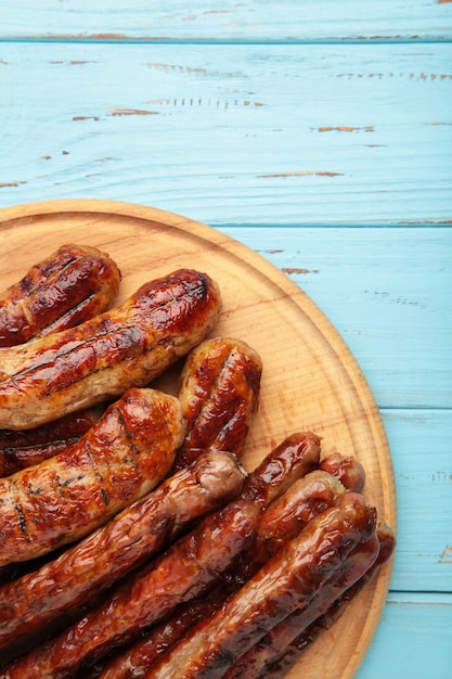 Gegrillte Würste auf Holzbrett auf blauer Oberfläche