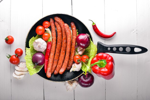 Gegrillte Würste in einer Pfanne mit frischem Gemüse Holzoberfläche Draufsicht