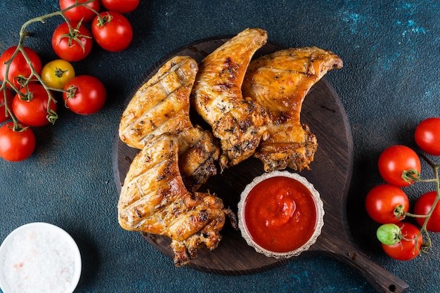 Gegrillte würzige Hähnchenflügel mit Ketchup auf einer schwarzen Platte auf dunklem Schieferstein oder Betonhintergrund Draufsicht mit Kopierraum BBQ-Konzept