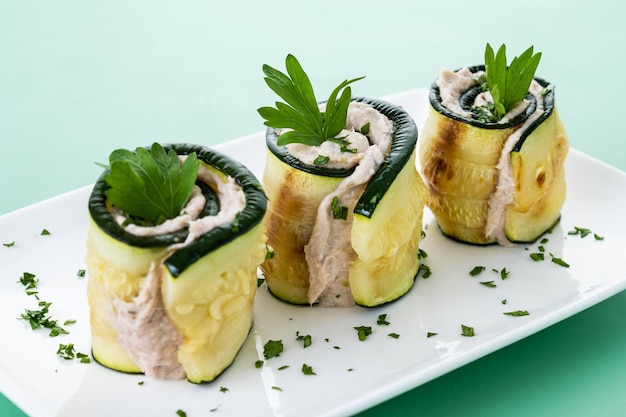 Foto gegrillte zucchini-rollen mit thunfisch und frischkäse auf grünem hintergrund