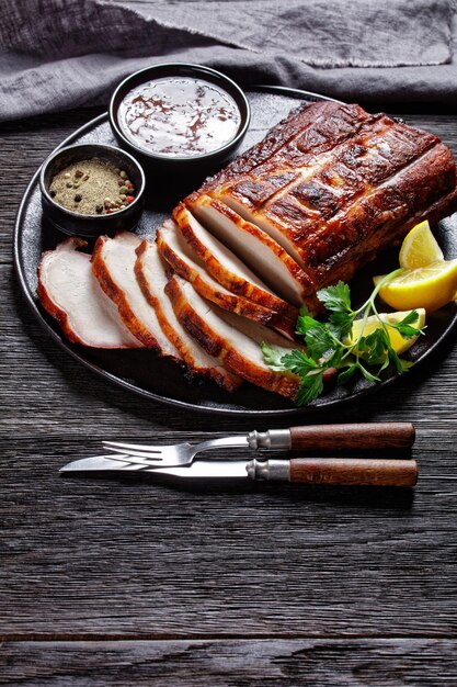 Gegrillter BBQ-Schweinebraten in Scheiben geschnitten auf einem Teller mit Gabel und Messer, vertikale Ansicht von oben