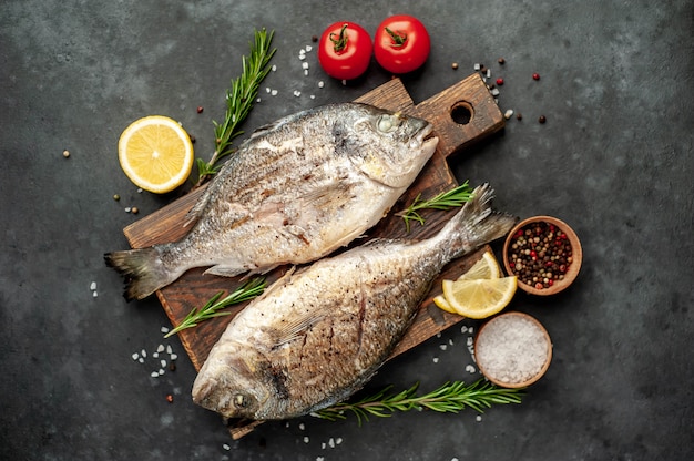 Gegrillter Dorado-Fisch auf einem Schneidebrett mit Gewürzen und Zitrone auf einem Steinhintergrund