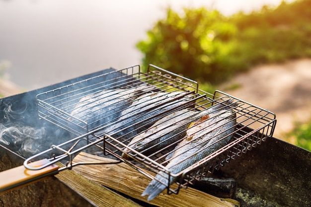 Gegrillter Fisch mit Gewürzen in Flammen. Fischgrill im Garten im Freien an einem warmen, sonnigen Tag.