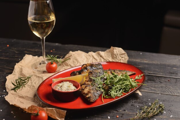 Gegrillter Fisch mit Zitrone und einem Rosmarinzweig. In einer roten Platte auf einem Holztisch