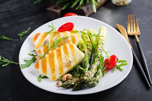 Gegrillter Halloumi-Käsesalat mit Tomaten und Spargel auf Teller auf dunklem Hintergrund. Gesundes vegetarisches Essen.