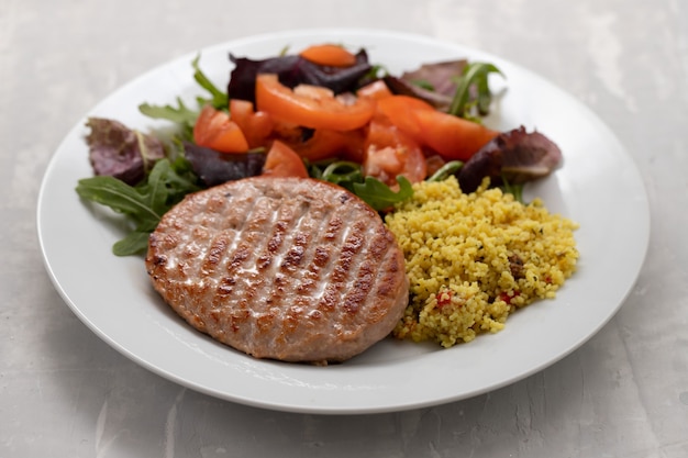 Gegrillter Hamburger mit Müsli und Salat auf weißem Teller