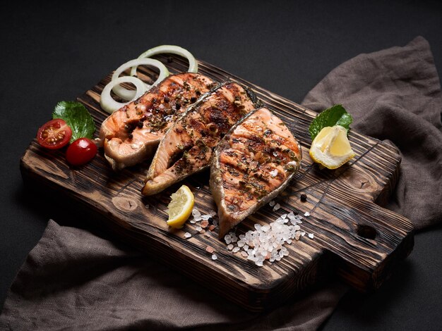 Gegrillter Lachs mit Zitronensalz Tomaten Zwiebeln und Kräutern auf Schneidebrett auf braunem Hintergrund