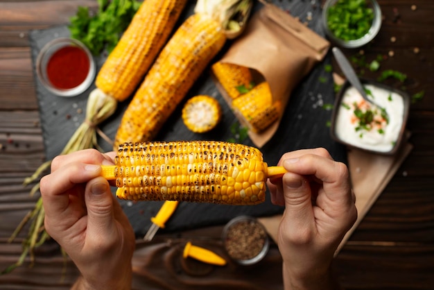 Foto gegrillter mais in kaukasischen händen auf dem hintergrund eines küchenholztisches