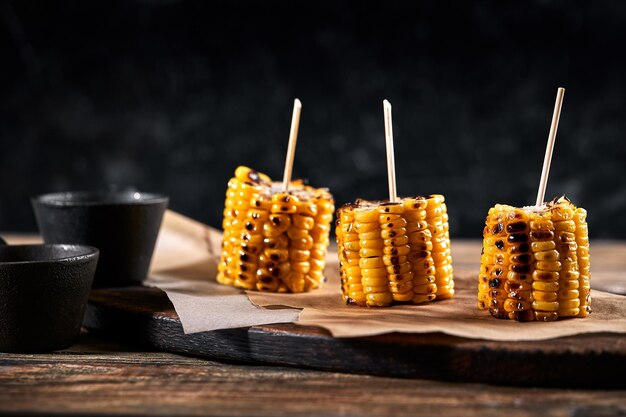 Gegrillter Mais mit Soßen auf einem hölzernen Hintergrund traditionelles amerikanisches Nebengericht dunkler Hintergrund Kopie