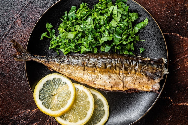 Gegrillter Makrelen-Scomber-Fisch auf einem Teller mit Gemüse und Zitrone Dunkler Hintergrund Draufsicht