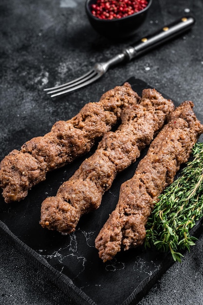 Gegrillter Schaschlik am Stiel, aus Rinder- und Lammfleisch, türkischer Adana-Kebab. Schwarzer Hintergrund. Ansicht von oben.