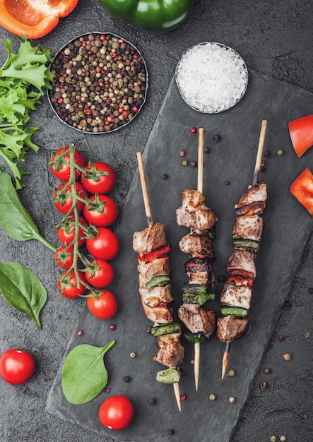 Gegrillter Schweinefleisch-Hühnchen-Kebab mit Paprika auf Steinschneidebrett mit Salz, Pfeffer und Tomaten auf Schwarz