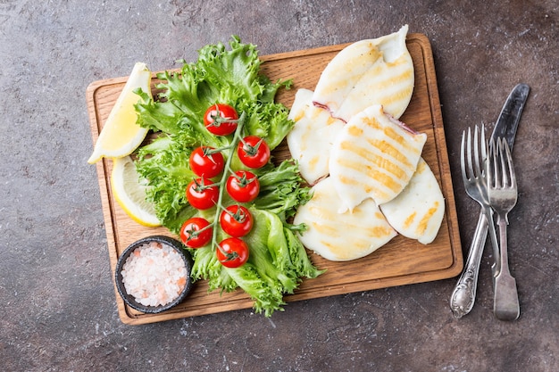 Gegrillter Tintenfisch mit Zitrone und Gemüse auf Holzschneidebrett über Dunkelheit