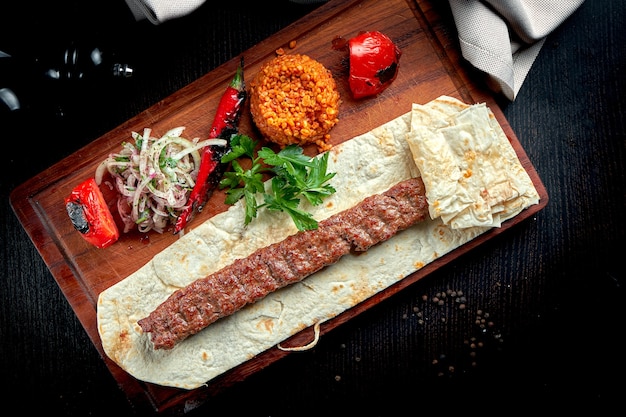 Gegrillter türkischer Lamm-Lula-Kebab mit gegrilltem Gemüse, Zwiebeln und Reis auf Holzbrett