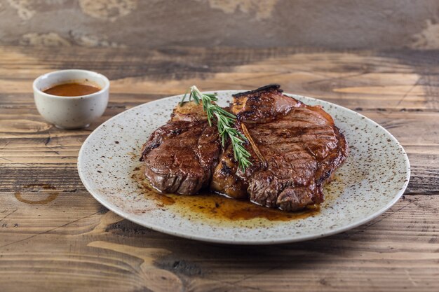 Gegrilltes Barbecue-Steakfilet aus rotem Rindfleisch mit Rosmarinzweig und scharfer Sauce auf weißem Teller.