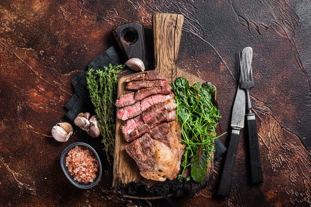 Gegrilltes Chuck Roll Beefsteak mit Salat auf Holzbrett Dunkler Hintergrund Ansicht von oben