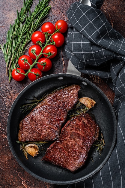 Gegrilltes Denver-Rindfleischsteak in einer Pfanne mit Rosmarin. Dunkler Hintergrund. Ansicht von oben.