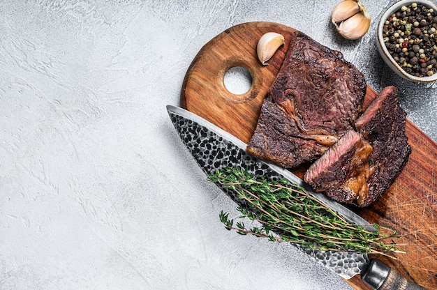 Gegrilltes erstklassiges Rib-Eye-Rindfleischsteak auf einem Holzbrett. Weißer Hintergrund. Ansicht von oben. Platz kopieren.