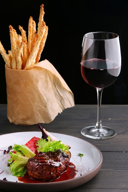 Gegrilltes Filet Mignon mit Gemüsesalat und Glas Rotwein und Grissini hautnah. Teller mit Filet Mignon auf Holztisch