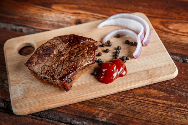 Gegrilltes Fleisch mit Gewürzen und Tomatensauce auf einem abgenutzten hölzernen Hintergrund