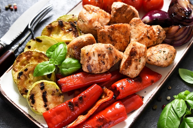 Gegrilltes Fleisch- und Gemüseset: Tomaten, Zwiebeln, Zucchini, Paprika in einem Teller auf einer Betonoberfläche