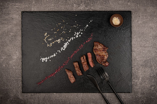 Gegrilltes Fleisch wird auf eine schwarze Steinschale gelegt Neben dem Messer Salz- und Pfefferstreuer