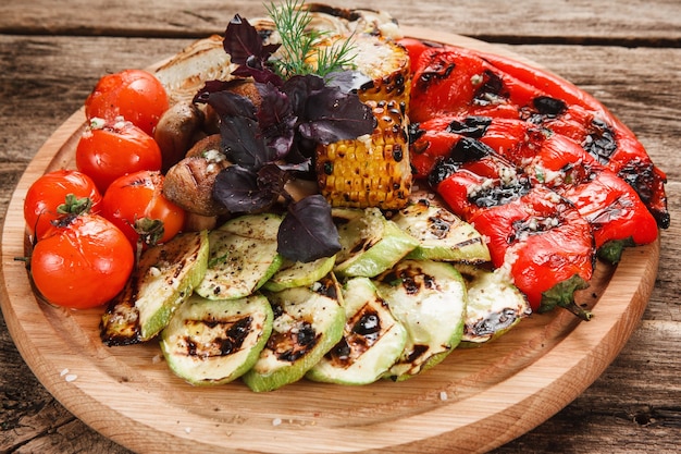 Gegrilltes Gemüse auf runder Platte serviert. Tomaten, Paprika, Zwiebeln, Zucchini, Mais und Pilze mit Basilikum dekoriert.