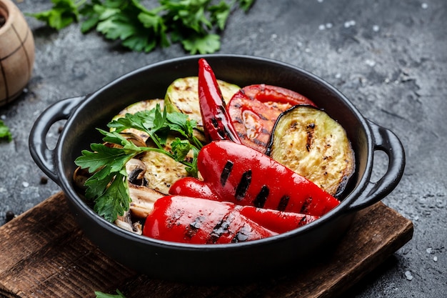 Gegrilltes Gemüse bunter Paprika, Zucchini, Auberginen mit Kräutern in einer gusseisernen Grillpfanne über Stein, Betonhintergrund. Hintergrund für Lebensmittelrezepte. Nahaufnahme