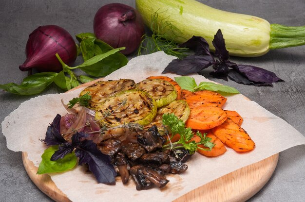 Gegrilltes gemüse und pilze auf einem holzbrett auf grauem hintergrund