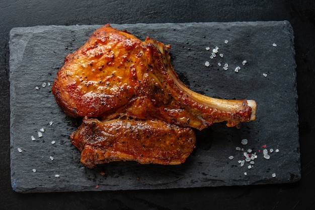 Gegrilltes gewürztes Filetschweinefleisch mit Knochen auf Schiefer auf dunklem Hintergrund. Nahaufnahme