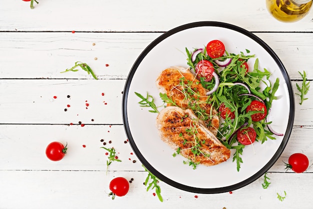 Gegrilltes Hähnchenfilet und frischer Gemüsesalat aus Tomaten, roten Zwiebeln und Rucola. Hühnerfleischsalat. Gesundes Essen. Flach liegen. Ansicht von oben.