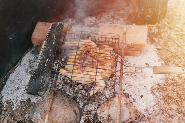 Gegrilltes Hähnchenfleisch auf schwelenden Kohlen oder Glut von einem Lagerfeuer auf dem Boden am Sommer- oder Herbsttag grillen unter Campingbedingungen Überleben auf dem Land und wildes rustikales Leben