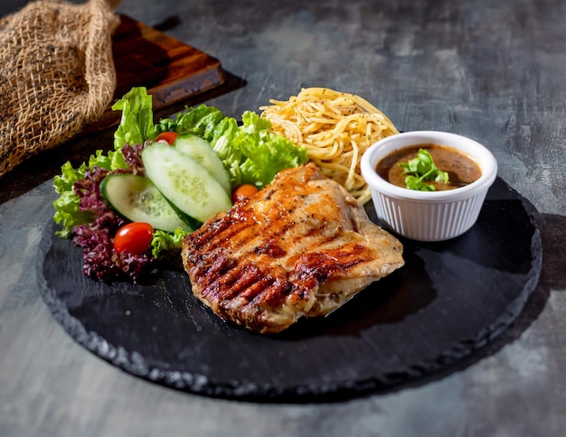 Gegrilltes Hähnchensteak ohne Knochen mit Chili-Sauce-Salatnudeln in einer Tellerseitenansicht auf dunklem Hintergrund