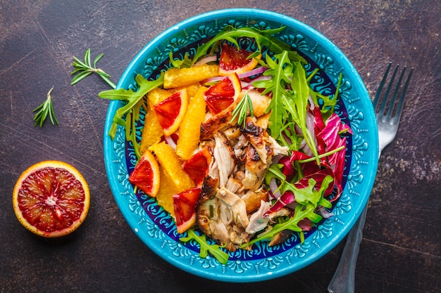 Gegrilltes Hühner- und Orangensalat mit Arugula in der blauen Platte auf weißem Hintergrund.