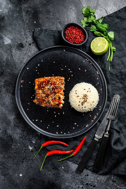 Gegrilltes japanisches Teriyaki-Lachsfilet, glasiert in köstlicher Sauce mit einer Beilage Reis. Schwarze Oberfläche. Draufsicht