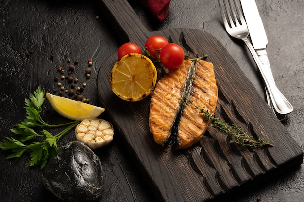 Gegrilltes Lachsfilet mit Kirschtomaten, Zitrone, Knoblauch und Thymian. Heißes Fischgericht auf einer Tafel.