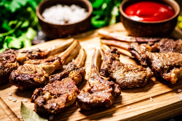 Gegrilltes Lammkarree auf einem Schneidebrett mit Petersilie und Tomatensoße