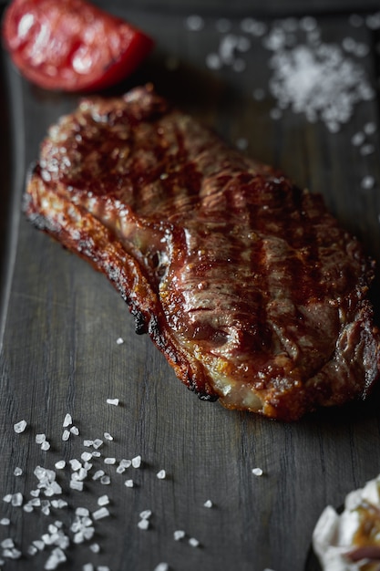 Gegrilltes Lendensteak serviert mit Knoblauch und Tomate auf Holzbrett, Detailansicht, Hochformat