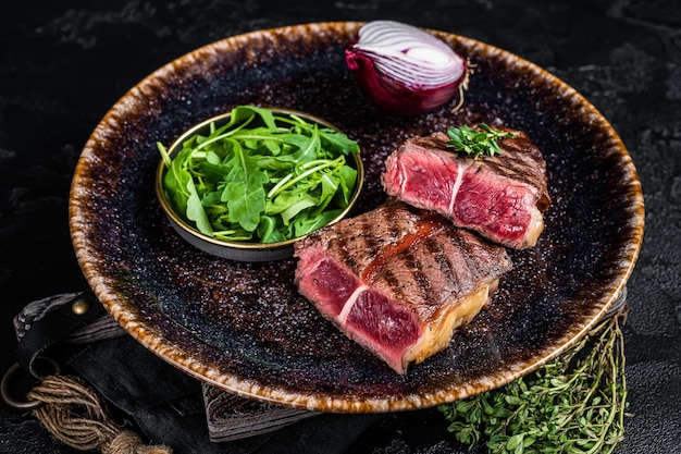 Gegrilltes Oyster Top Blade Rindersteak auf einem Teller mit Salat Schwarzer Hintergrund Draufsicht