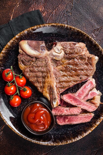 Gegrilltes Porterhouse-Rindfleisch Steak gekocht t Bone in einem Teller mit Tomate Dunkler Hintergrund Ansicht von oben