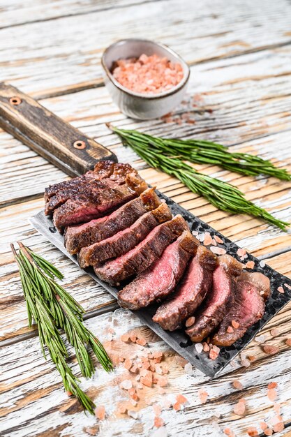 Gegrilltes Ramp Cap Steak auf einem Fleischerbeil. Weißer hölzerner Hintergrund. Draufsicht.