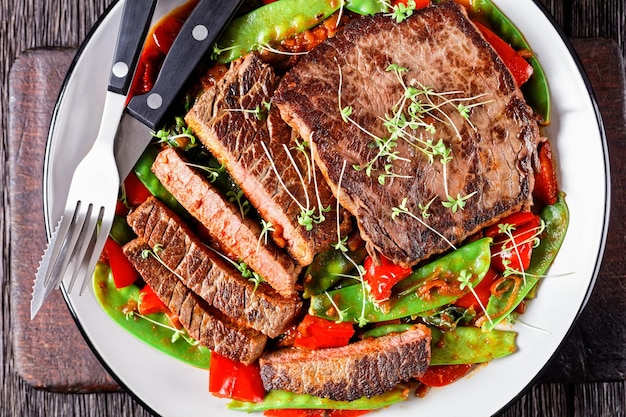 Gegrilltes Rinderflankensteak, serviert mit Ragout aus in Tomatensoße geschmortem Gemüse und Kräutern, roten Paprikaschoten und Thymian in der Nähe