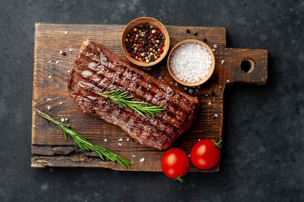 Foto gegrilltes rindersteak auf einem holzbrett mit gewürzen auf einem steinhintergrund